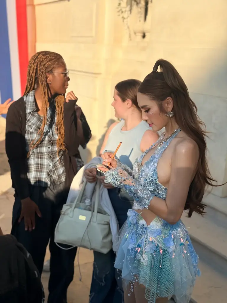 Jeune femme en robe bleue scintillante signant un autographe devant plusieurs personnes.