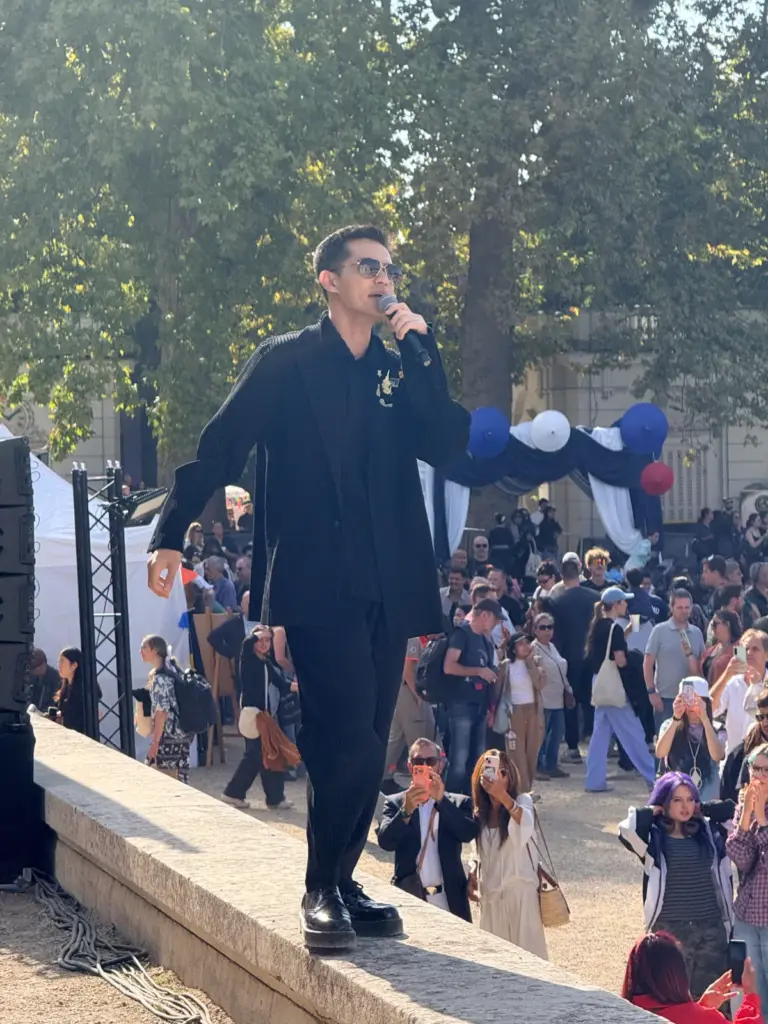 Chanteur vêtu de noir et portant des lunettes de soleil se produisant en extérieur, un micro à la main.
