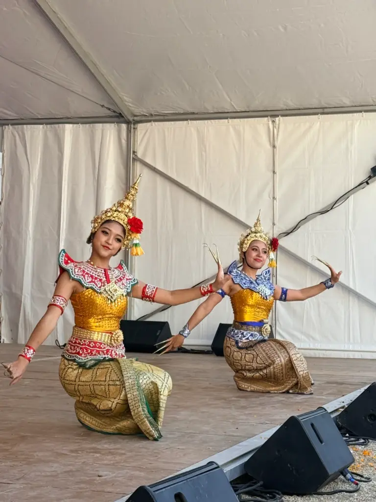 Deux danseuses en costumes traditionnels dorés présentent une chorégraphie sur une scène couverte.