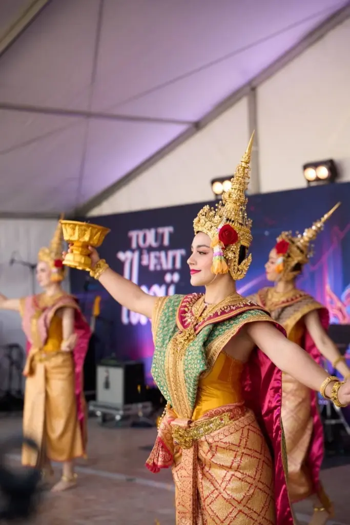 Danseuse en costume traditionnel thaïlandais richement orné, portant une coiffe dorée et réalisant une chorégraphie sur la scène du festival Tout à fait Thaï.