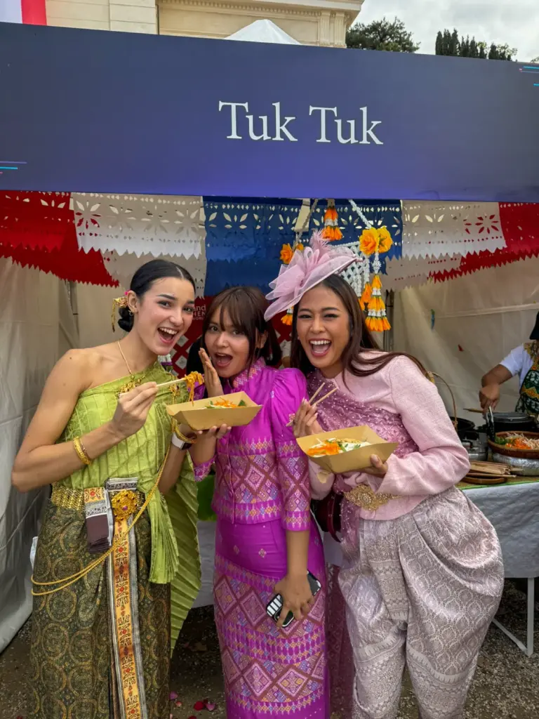 Trois femmes en tenues thaïlandaises colorées dégustent des spécialités culinaires dans un espace de restauration.