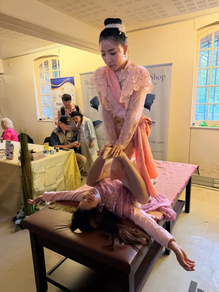 Démonstration de massage traditionnel thaïlandais avec une personne allongée sur une table et une praticienne en tenue rose.