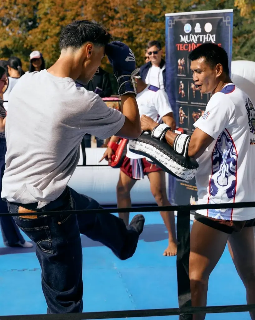 Deux pratiquants de Muay Thaï réalisent une démonstration technique sur un ring devant le public.