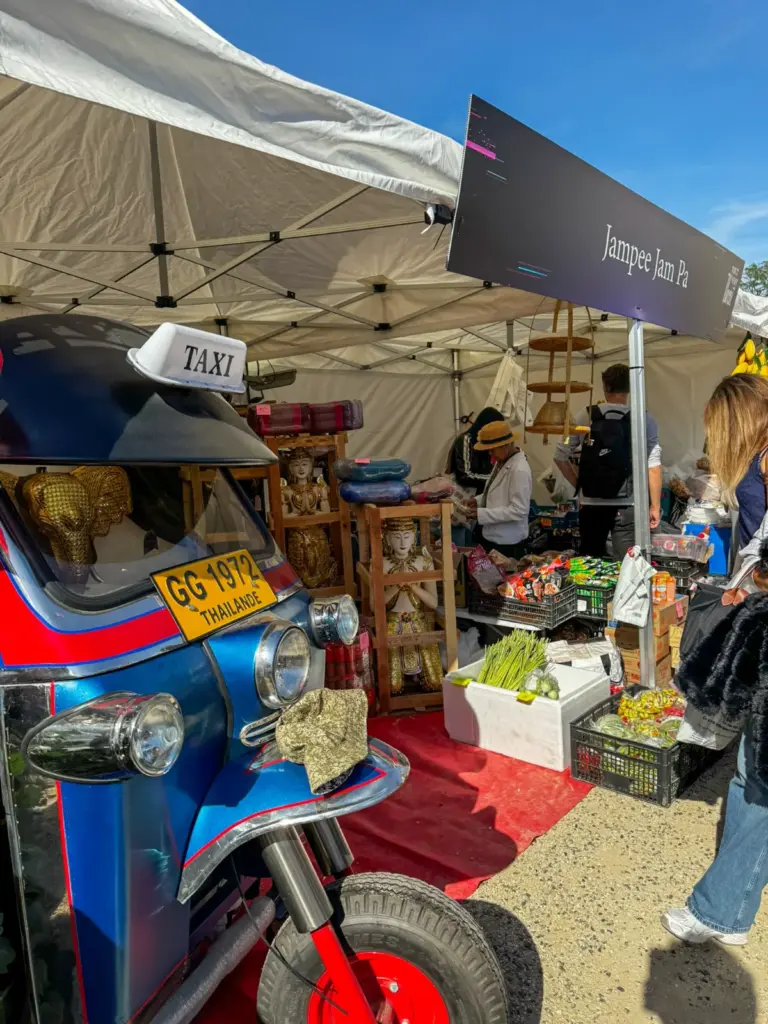 Gros plan sur l'avant d'un tuk-tuk thaïlandais bleu et rouge exposé devant un stand de produits artisanaux.