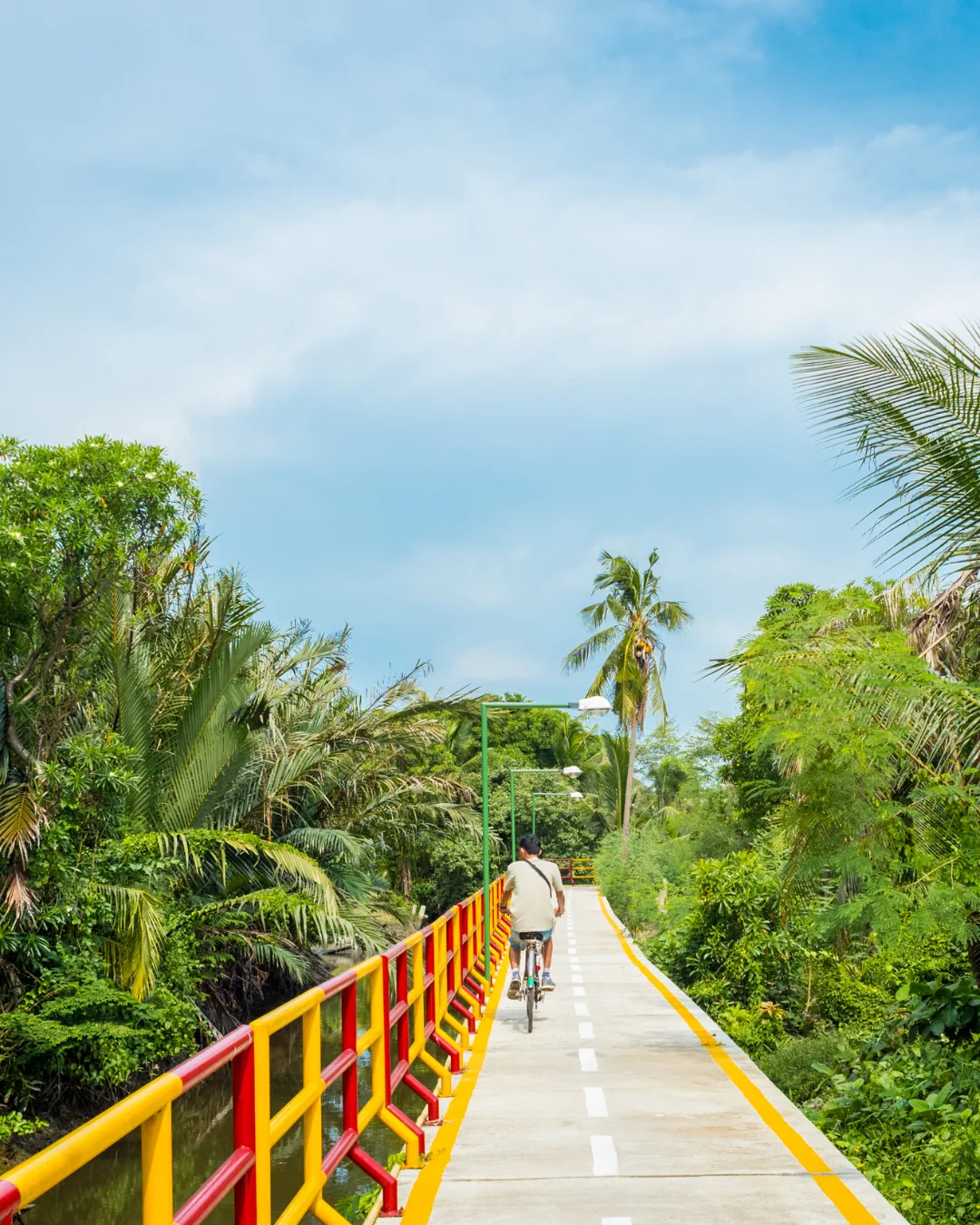 Longue passerelle aux garde-corps jaunes et rouges traversant un paysage tropical verdoyant sous un ciel bleu.